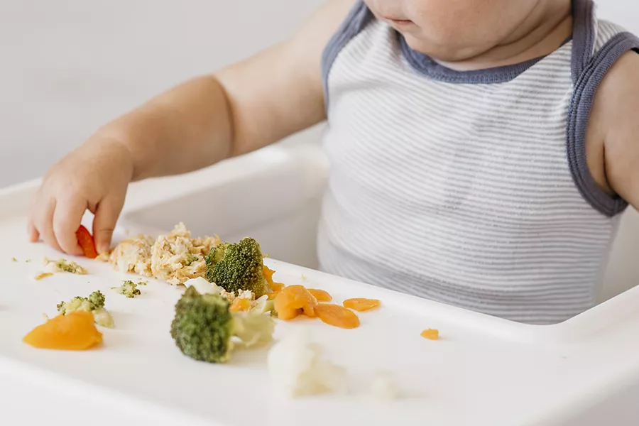 A baby eating pieces of broccoli and carrot