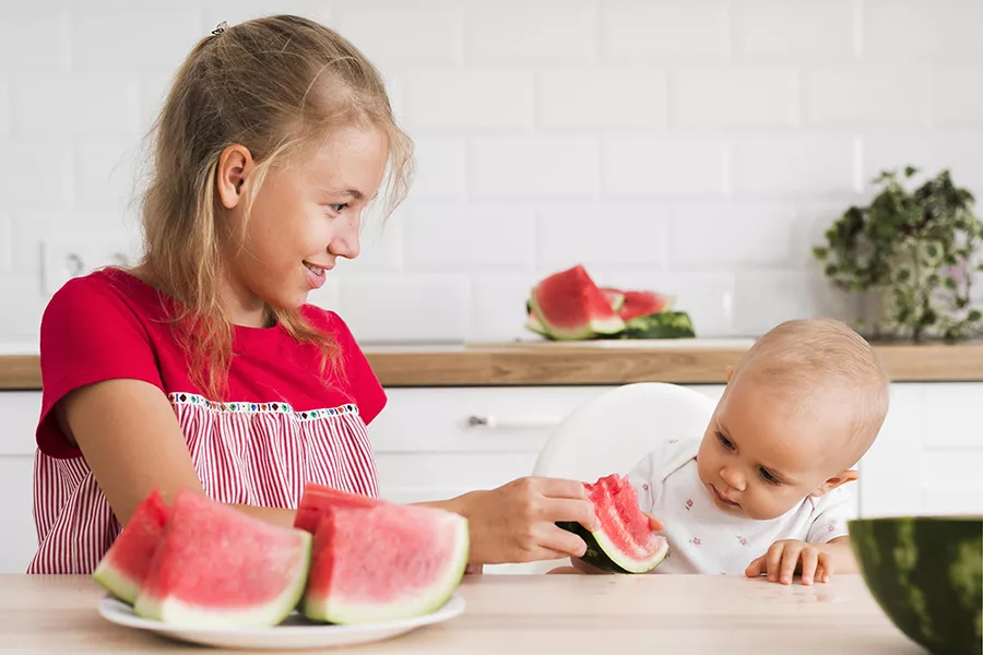 A girl and a baby eating watermelon together