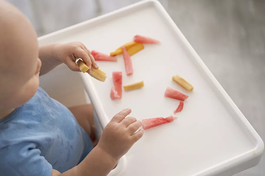 A baby eating a piece of fruit while sitting in a high chair