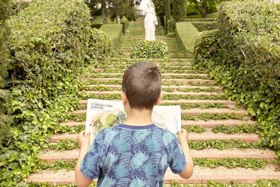 Child reading a map in front of some stairs and a statue full of plants