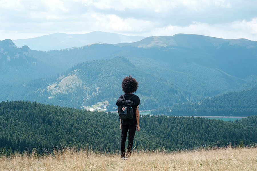 A hiker with a backpack standing on a hill admiring the valley below.