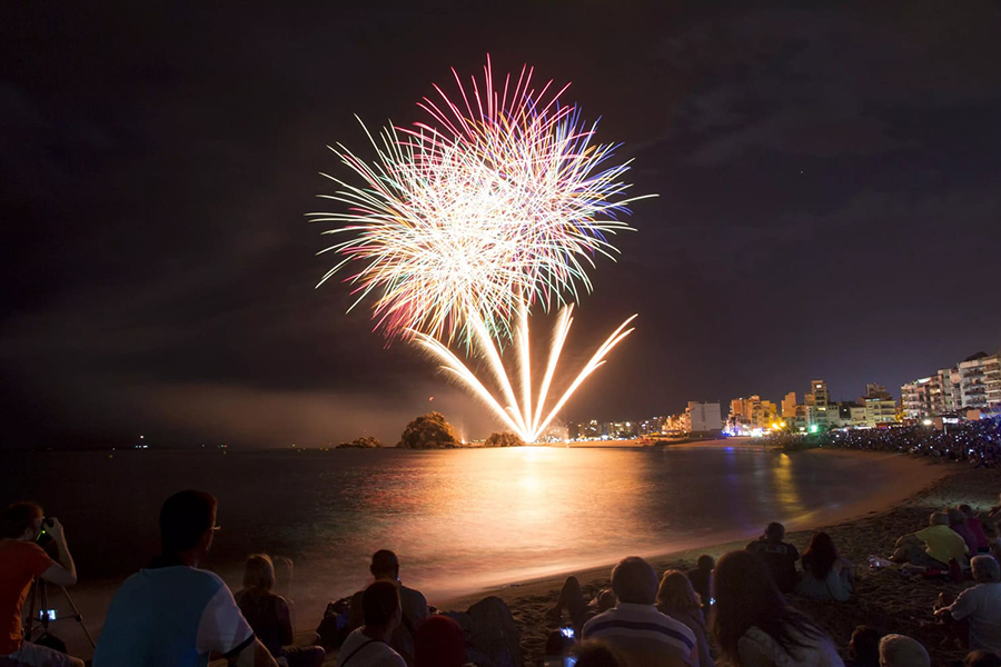 Fuegos artificiales de Blanes iluminan la playa por la noche.