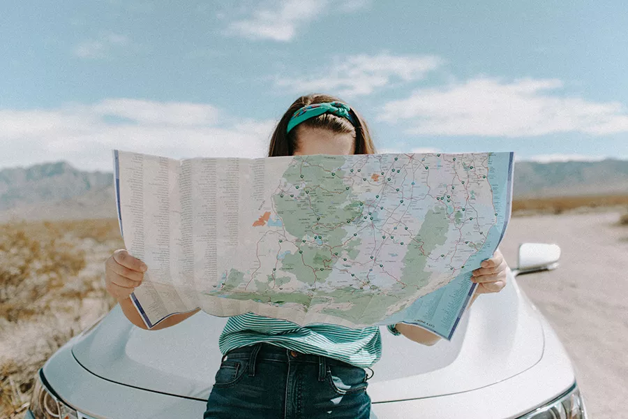 Person leaning on their car on a road in the middle of nature consulting a map