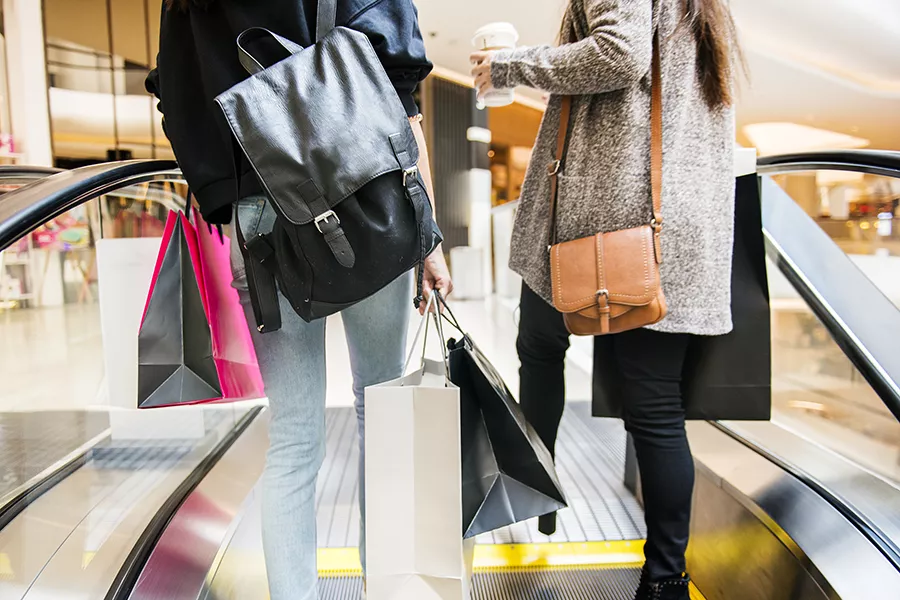 Two people going up an escalator with duty-free shopping bags