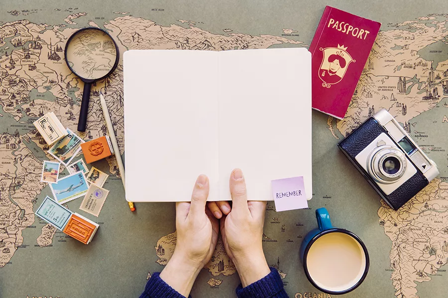 Hands holding a notebook above a map and various travel-related items such as a passport or camera